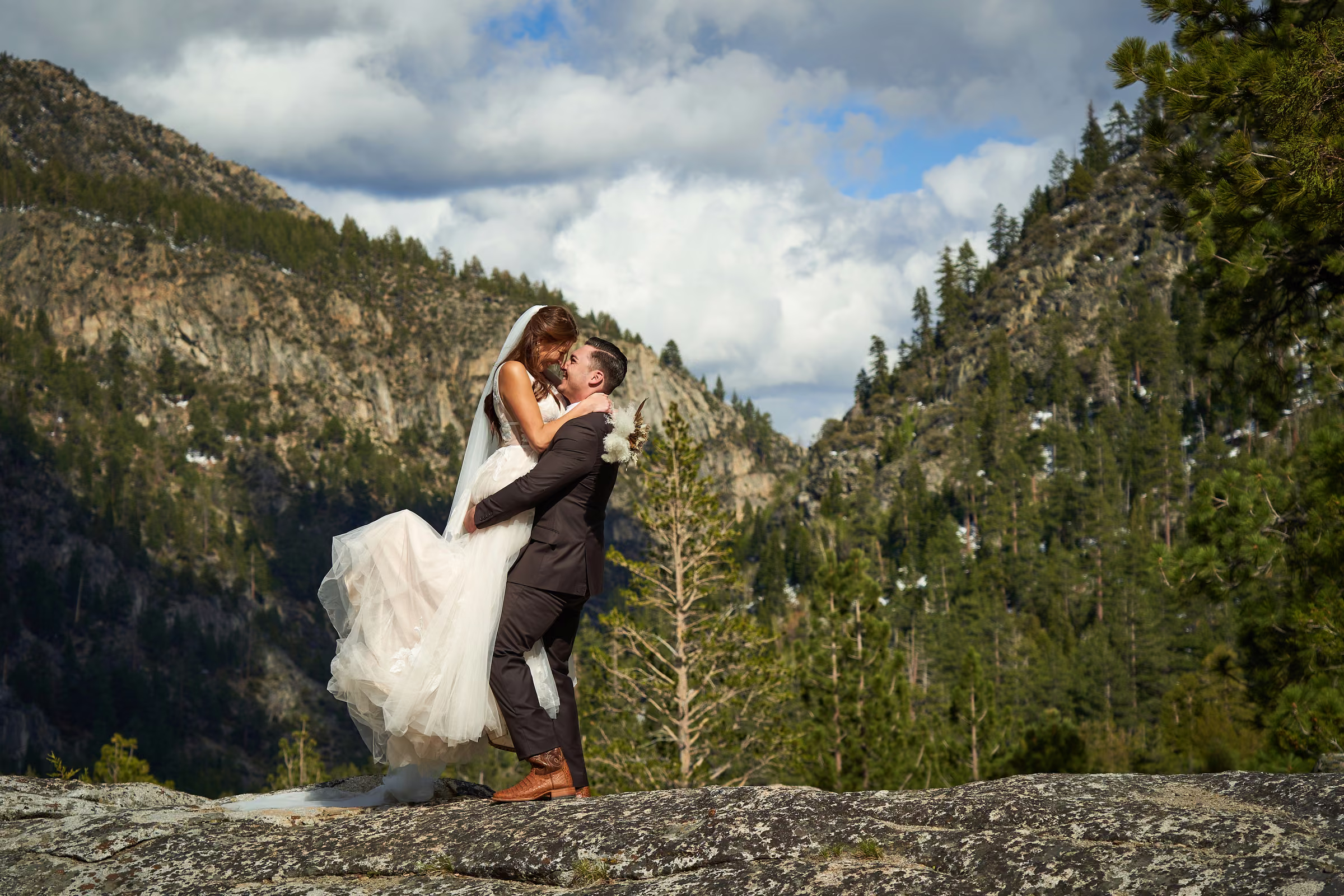 Joe lifts Gabby into his arms on the rock above the valley for a portrait after their ceremony, Hope Valley, California