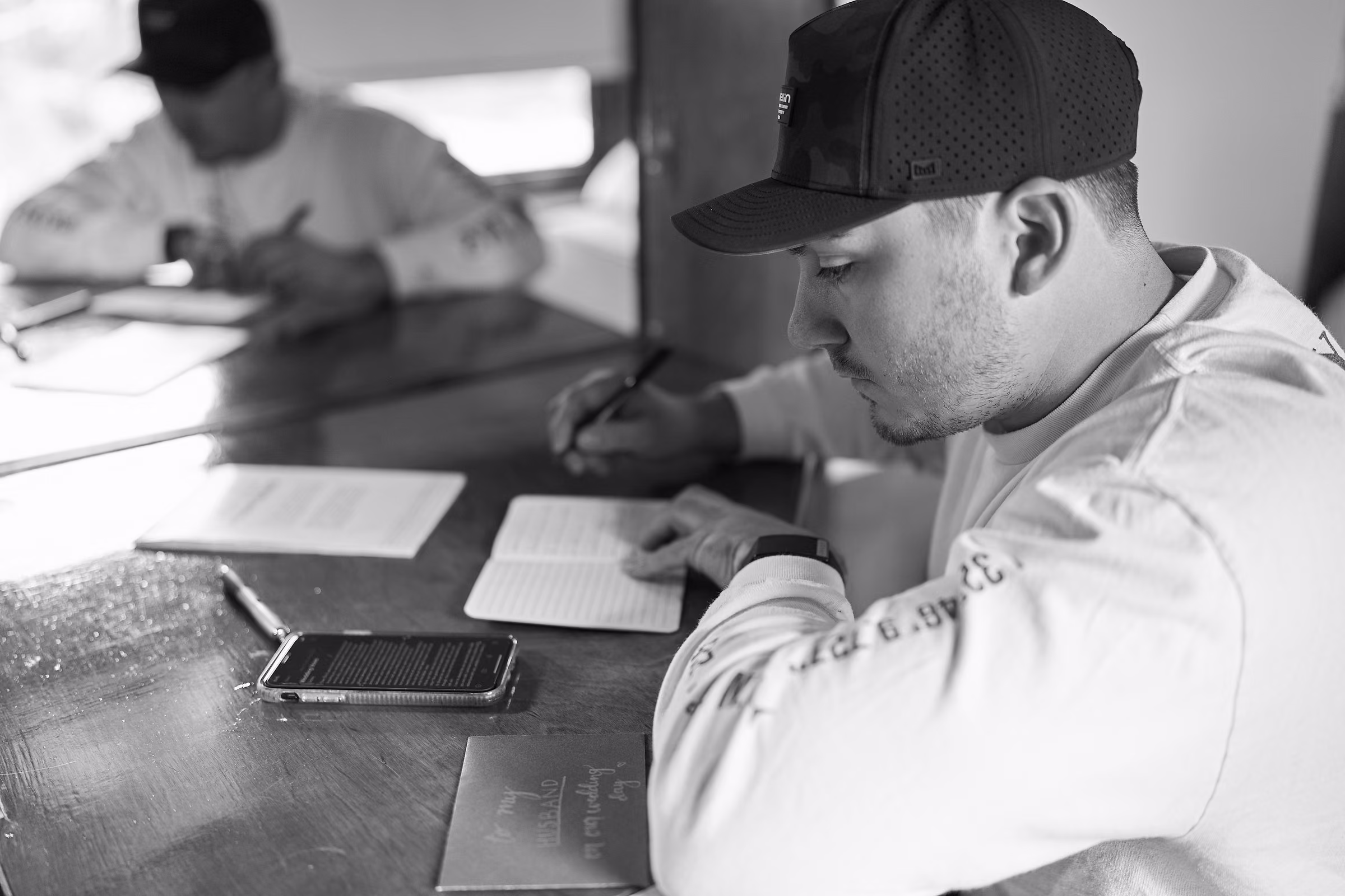 Joe leans over a table to write his wedding vows in a black and white photograph, Hope Valley, California