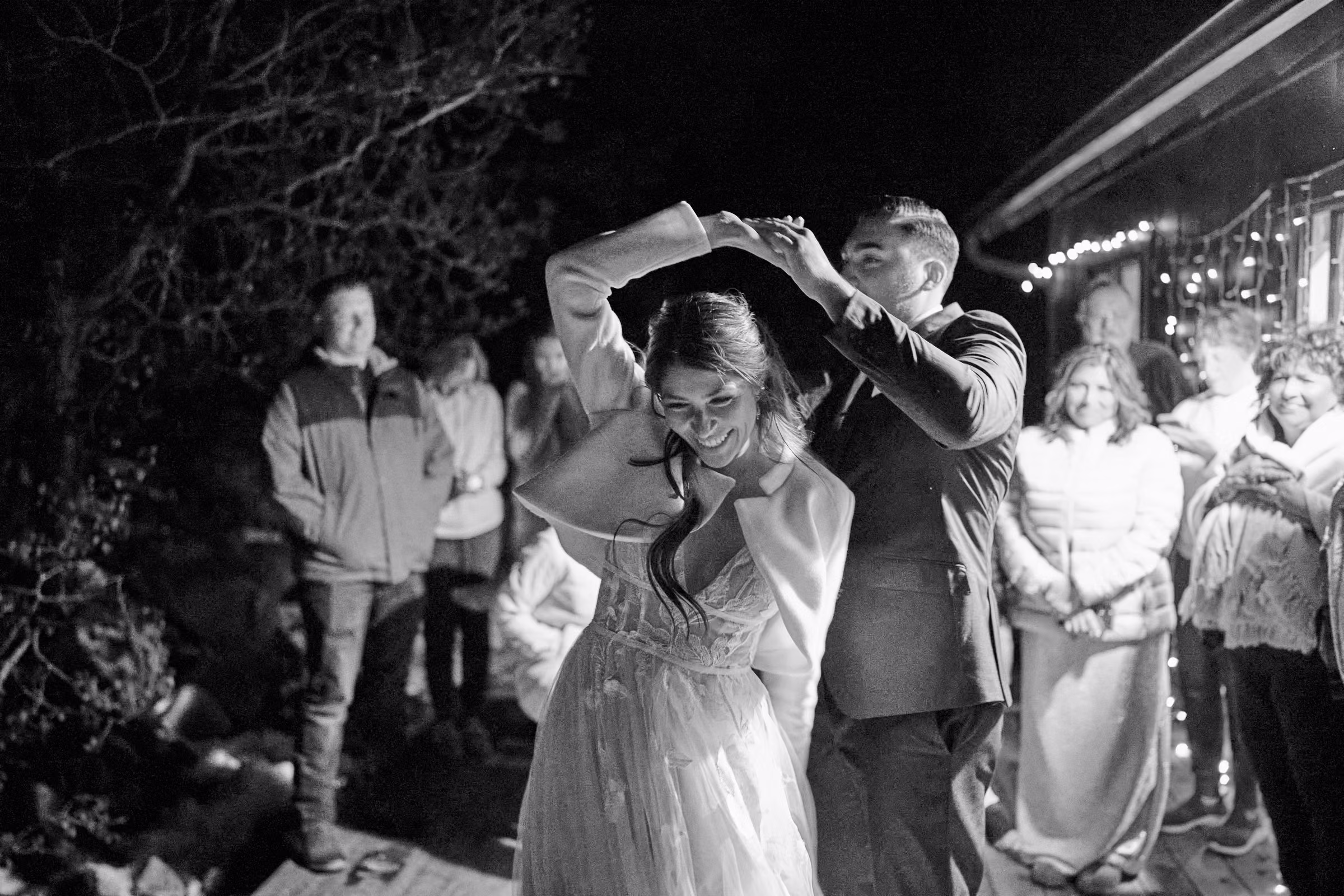 Joe twirls Gabby during their first dance on a small wooden deck outdoors as their family watches, Hope Valley, California
