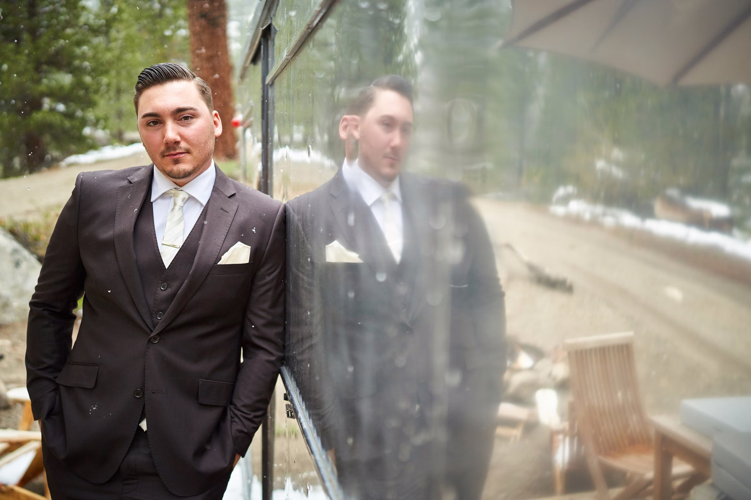 Joe stands in his wedding suit beside the silver trailer, with his reflection in its side, Hope Valley, California