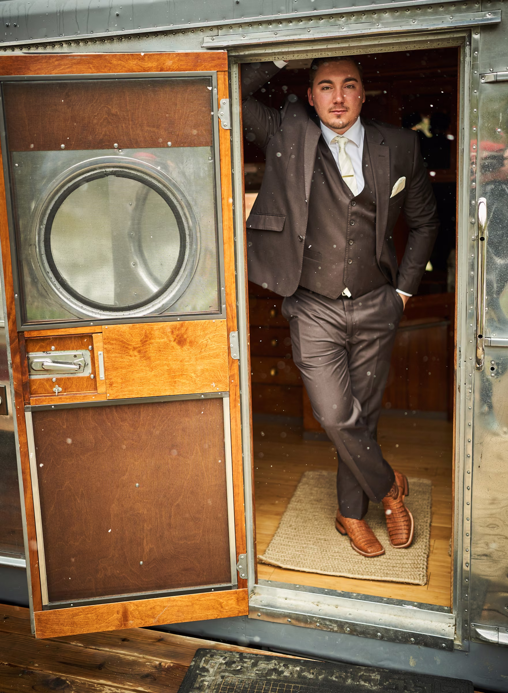 Joe stands in the open doorway of the silver trailer in his wedding suit, Hope Valley, California