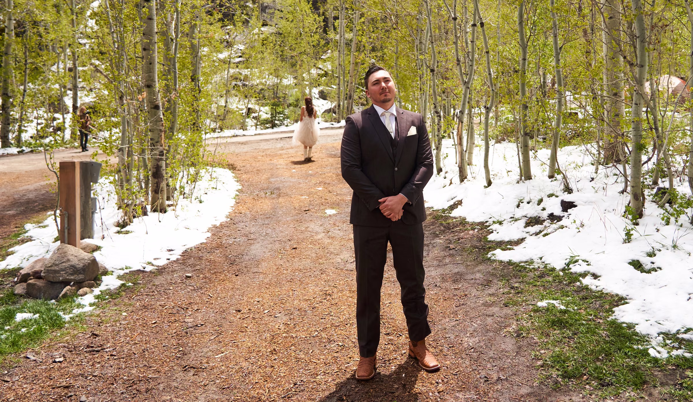 Joe waits on a wooded path with snow on the ground before seeing Gabby in her wedding dress, Hope Valley, California