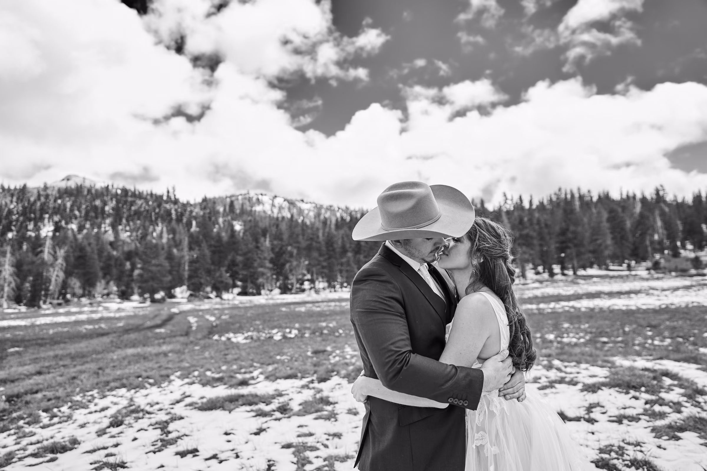 A black and white portrait of Joe and Gabby kissing in an open field with snow-covered mountains behind them, Hope Valley, California