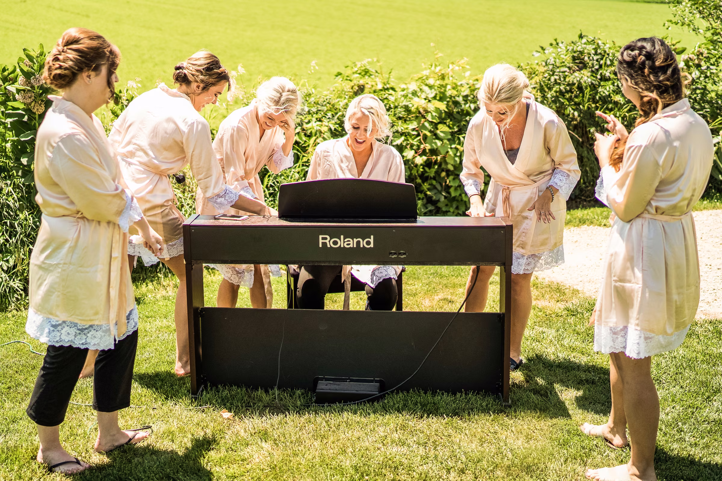 Katie and her bridesmaids in robes gather around a keyboard at the outdoor ceremony site