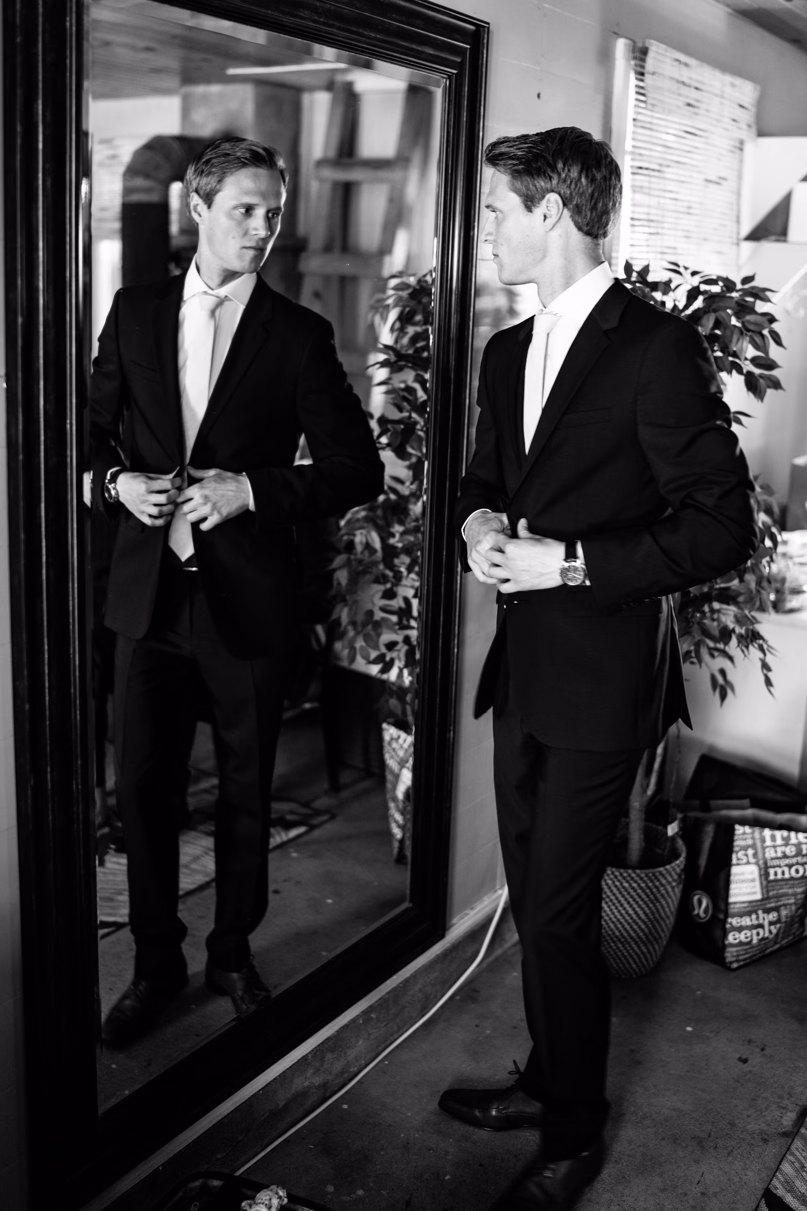 Tobias adjusts his suit while looking into a mirror in a rustic room