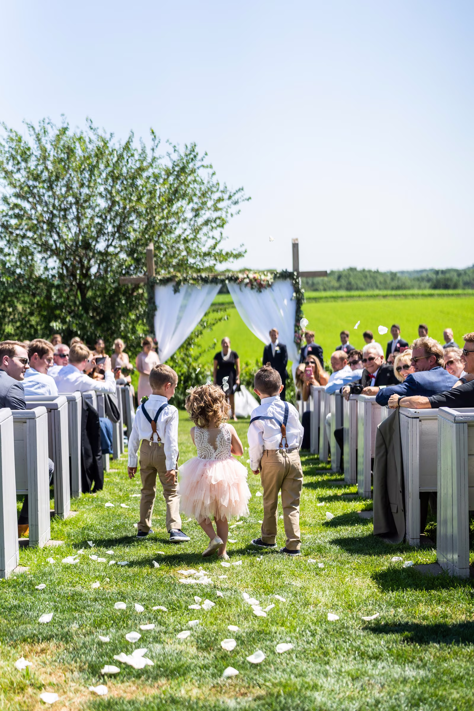 Katie walks toward the outdoor ceremony with her father between rows of white pews