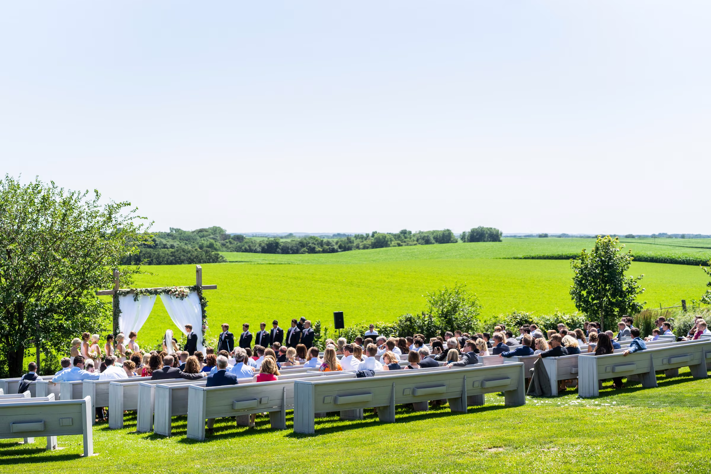 Wide view of guests seated in white outdoor pews overlooking green fields at Legacy Hill Farm