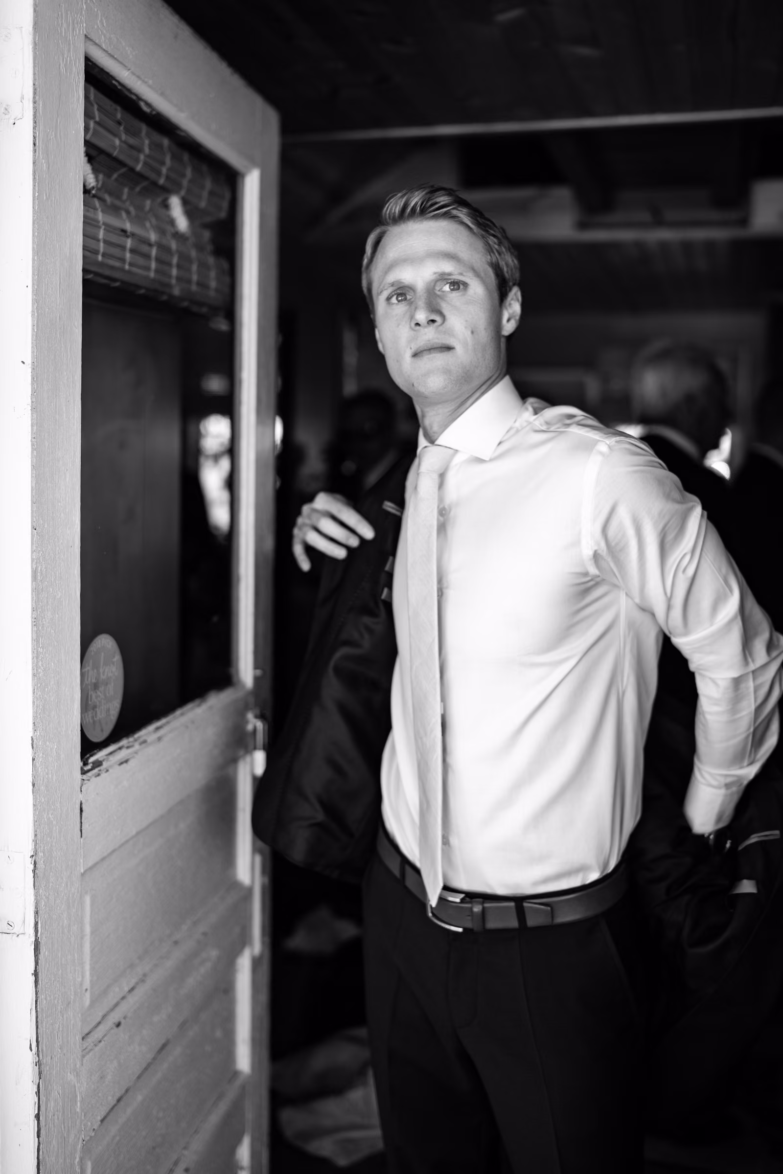 Black-and-white portrait of Tobias putting on his jacket in a doorway