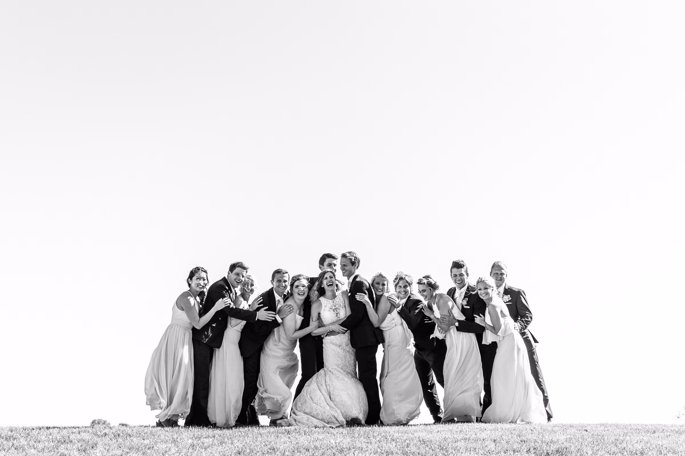 Black-and-white photograph of Katie, Tobias, and their wedding party hugging at the top of a hill