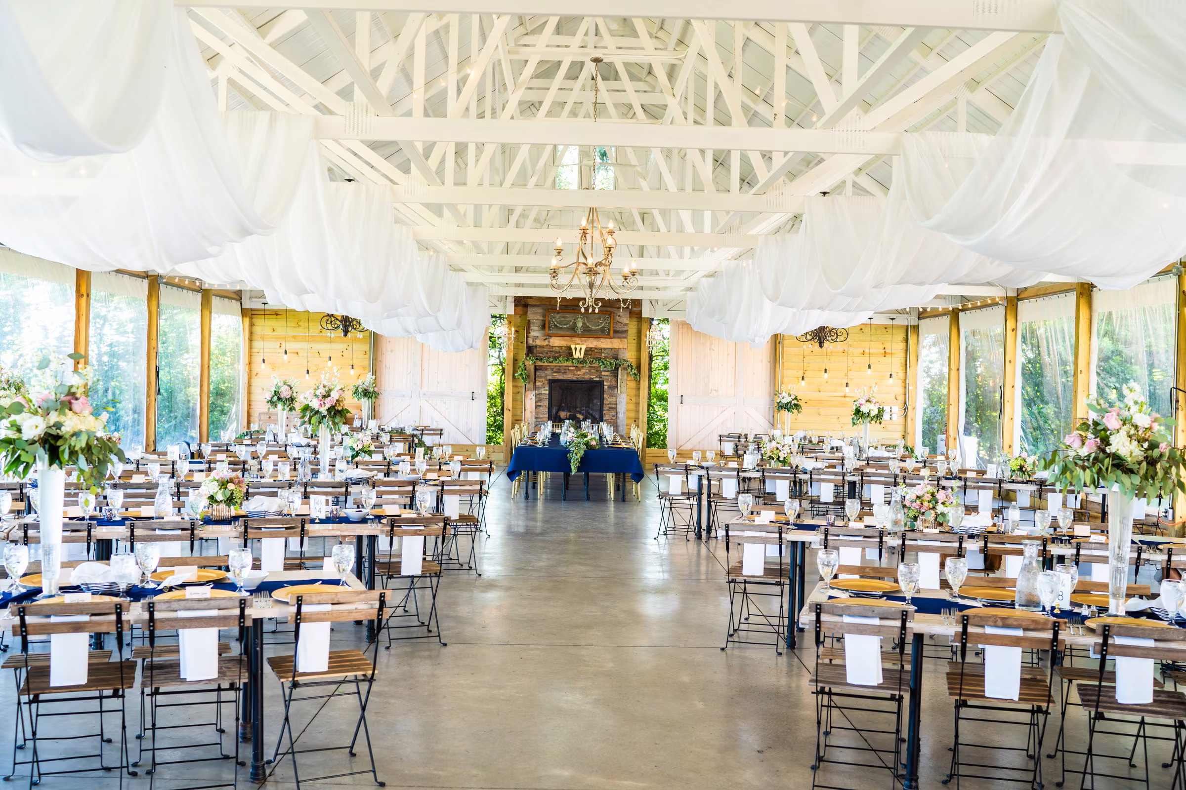 Wide view of the reception barn with tables set beneath white ceiling beams and drapery