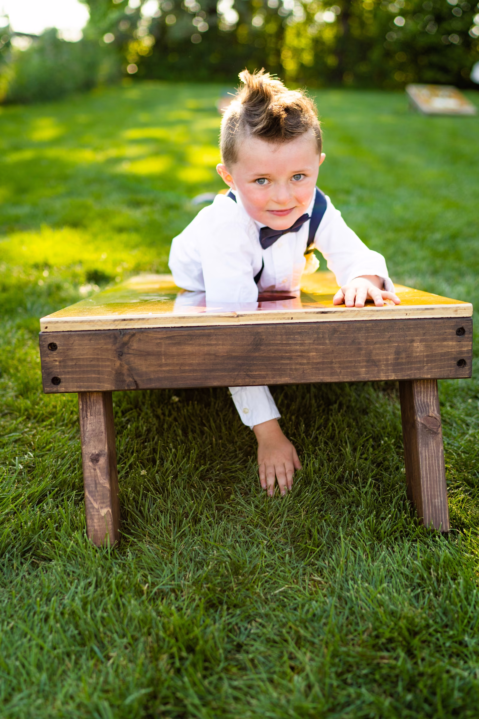 A young ring bearer reaches through the cornhole board to retrieve the beanbags