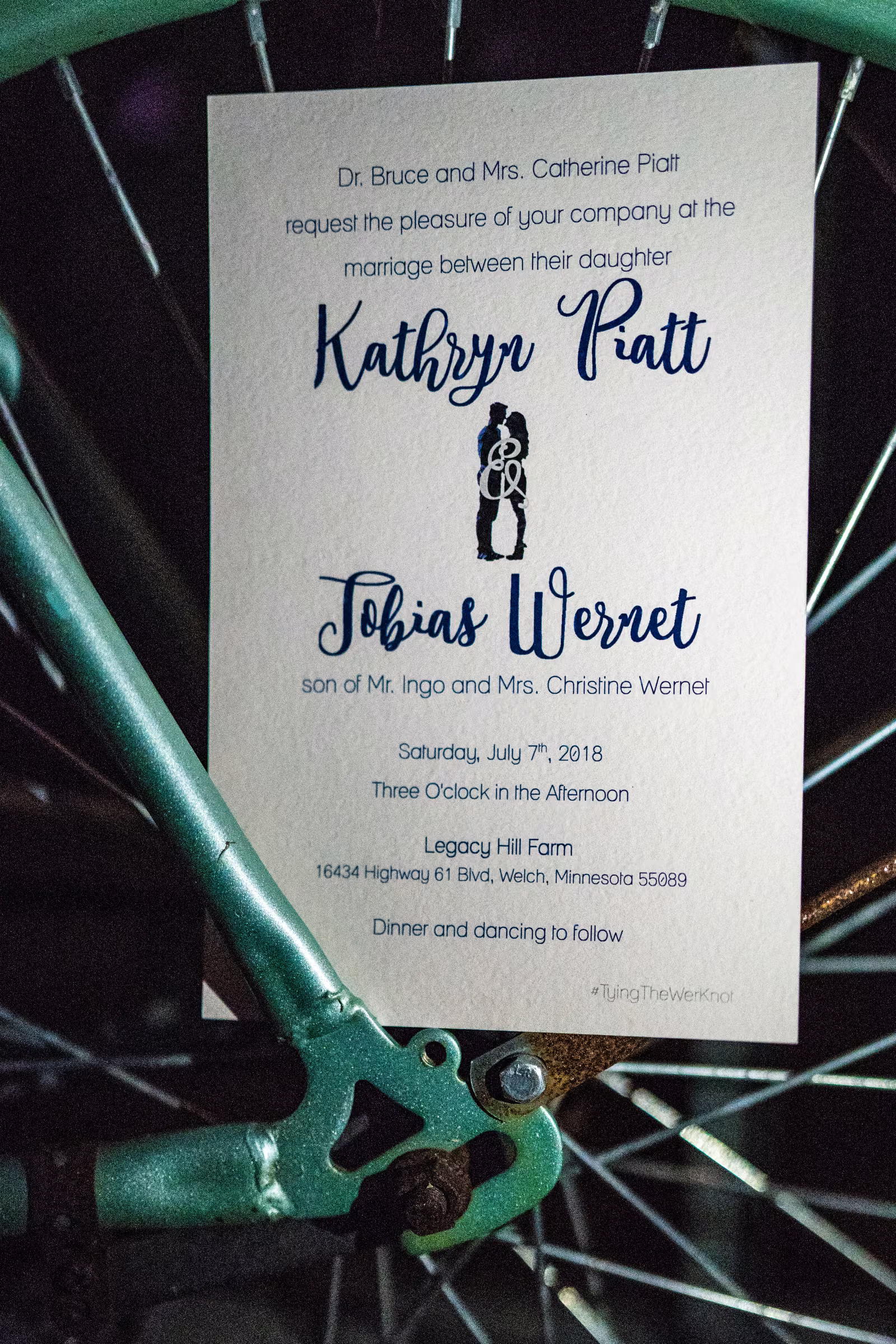 Kathryn Piatt and Tobias Wernet’s July 7, 2018 Legacy Hill Farm wedding invitation photographed against a bicycle wheel