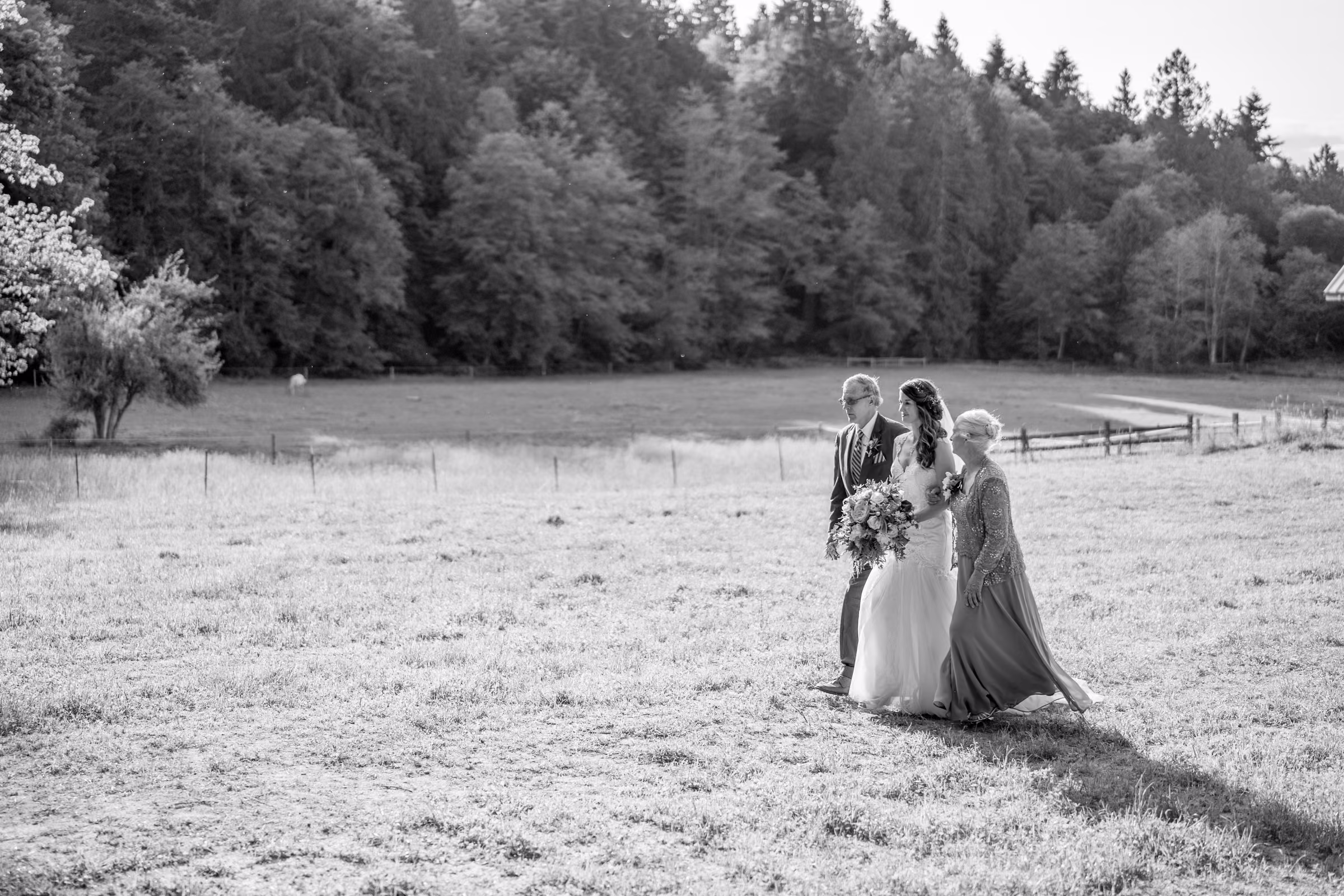 Kohleen walks across an open field with her parents toward the trees in a black and white photograph