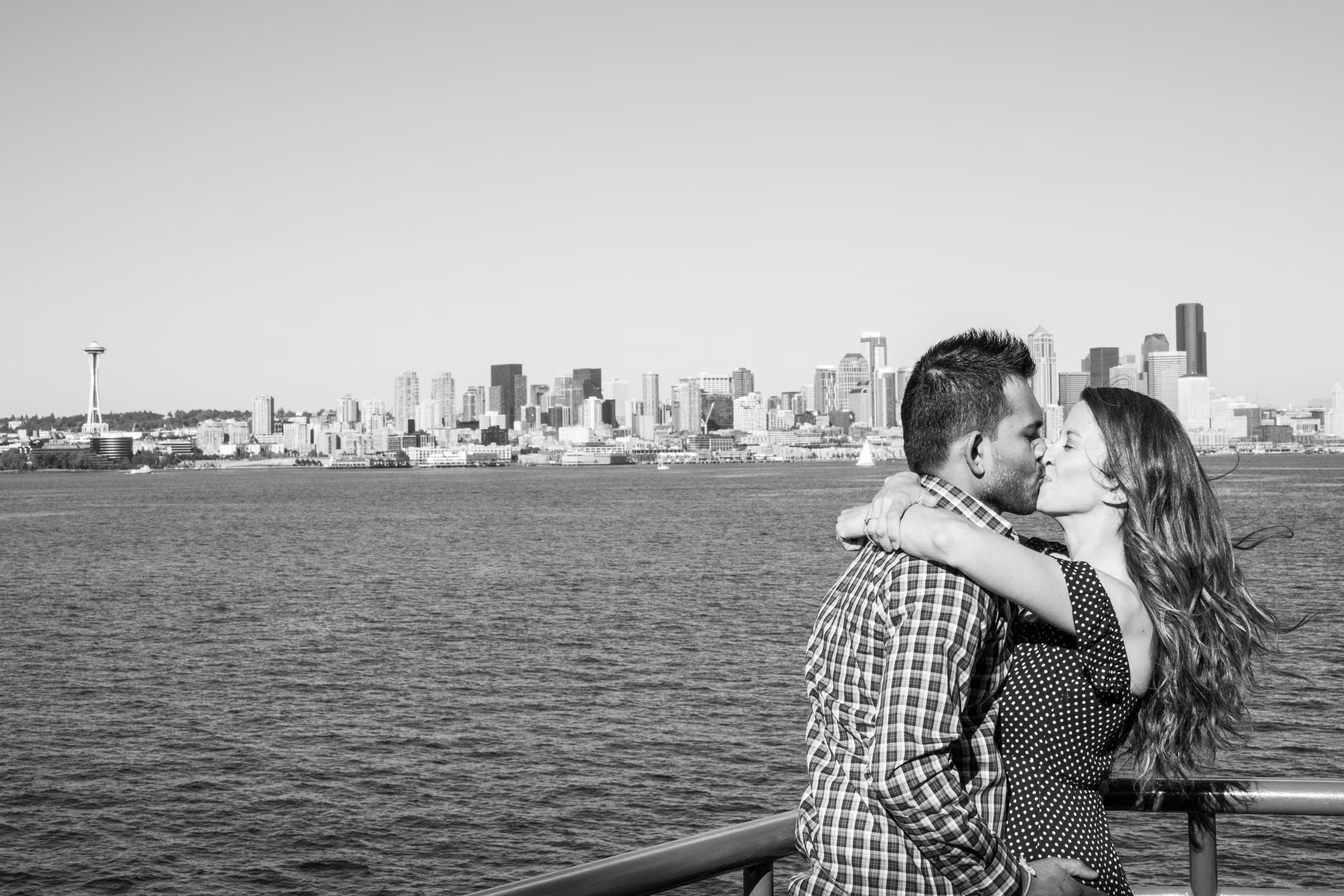Kohleen and Kash embrace on a ferry with the Seattle skyline across the water behind them