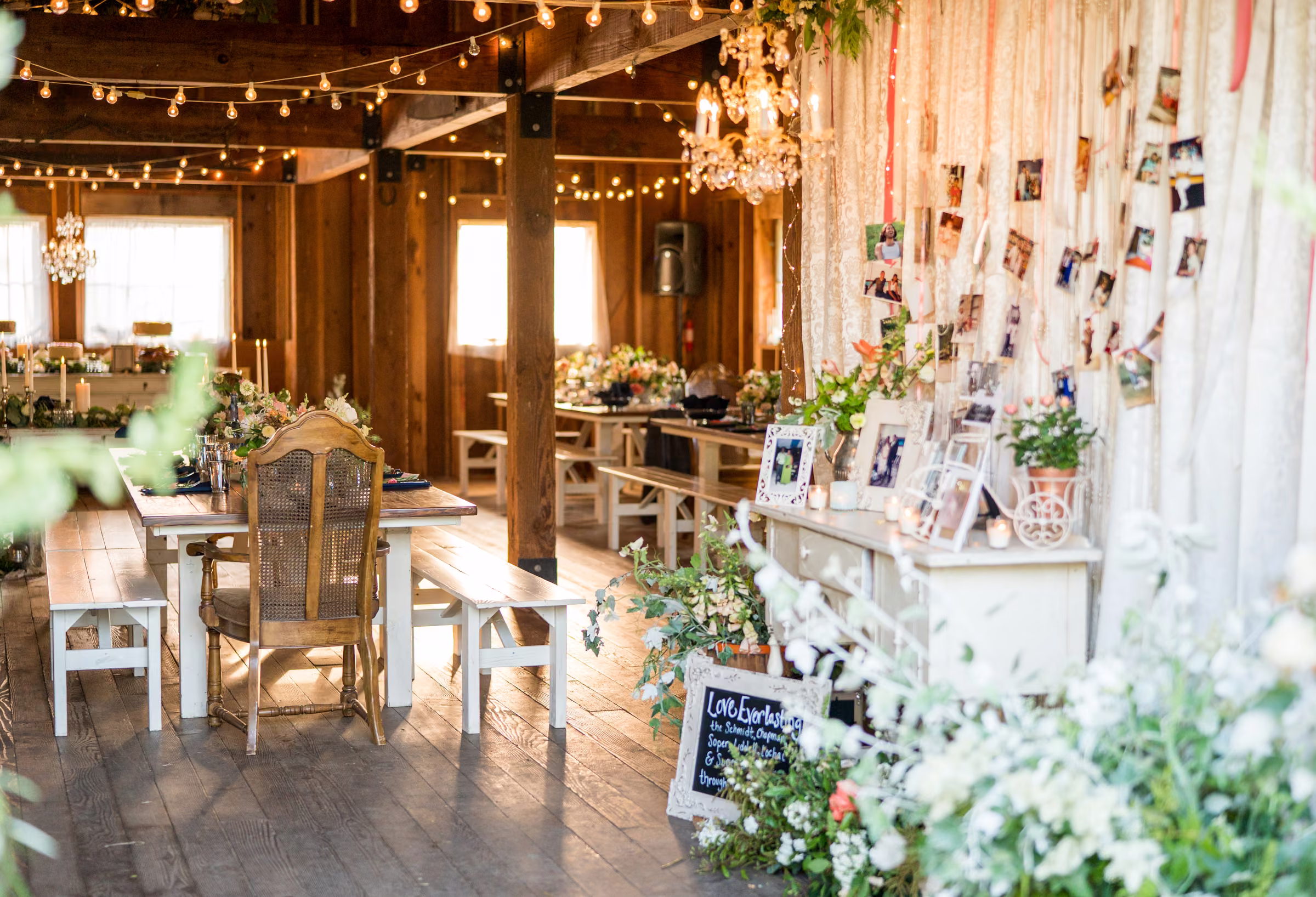 Warm string lights, flowers, and framed family photographs decorate the wooden barn interior