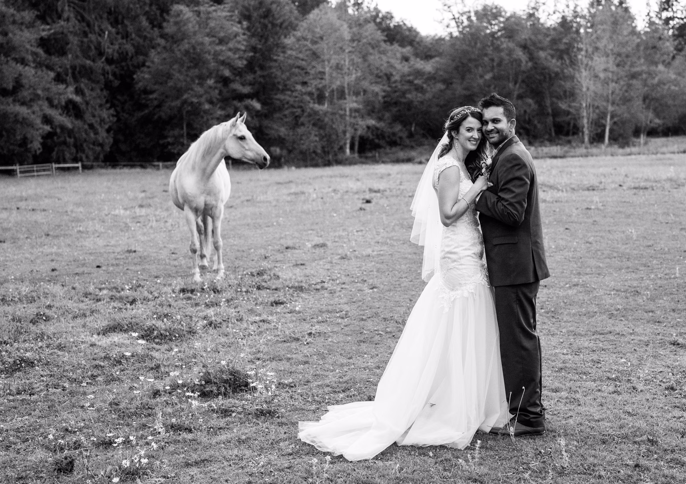 Kohleen and Kash pose in a field with a white horse standing behind them