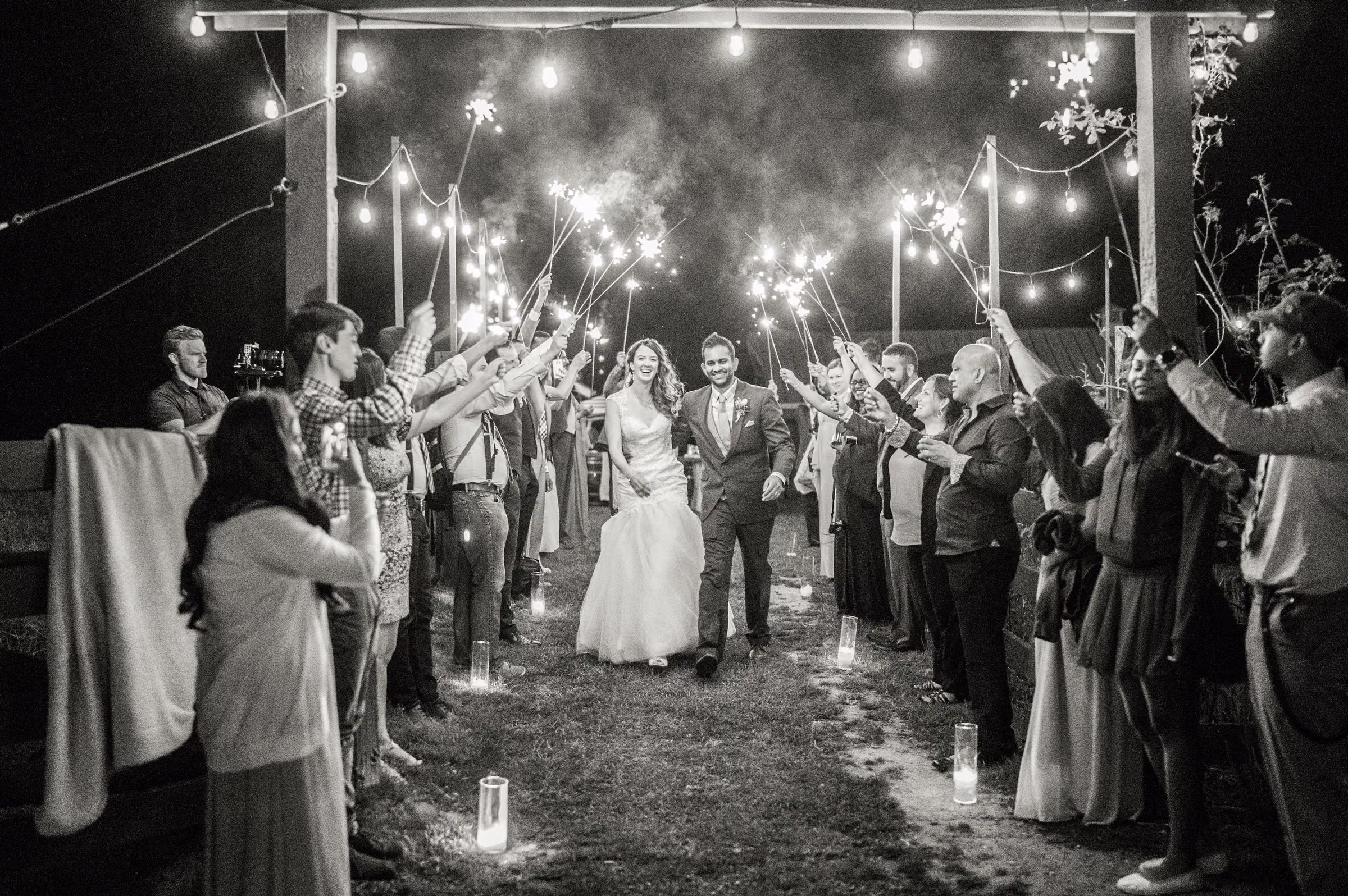 Kohleen and Kash walk between cheering guests holding sparklers at night