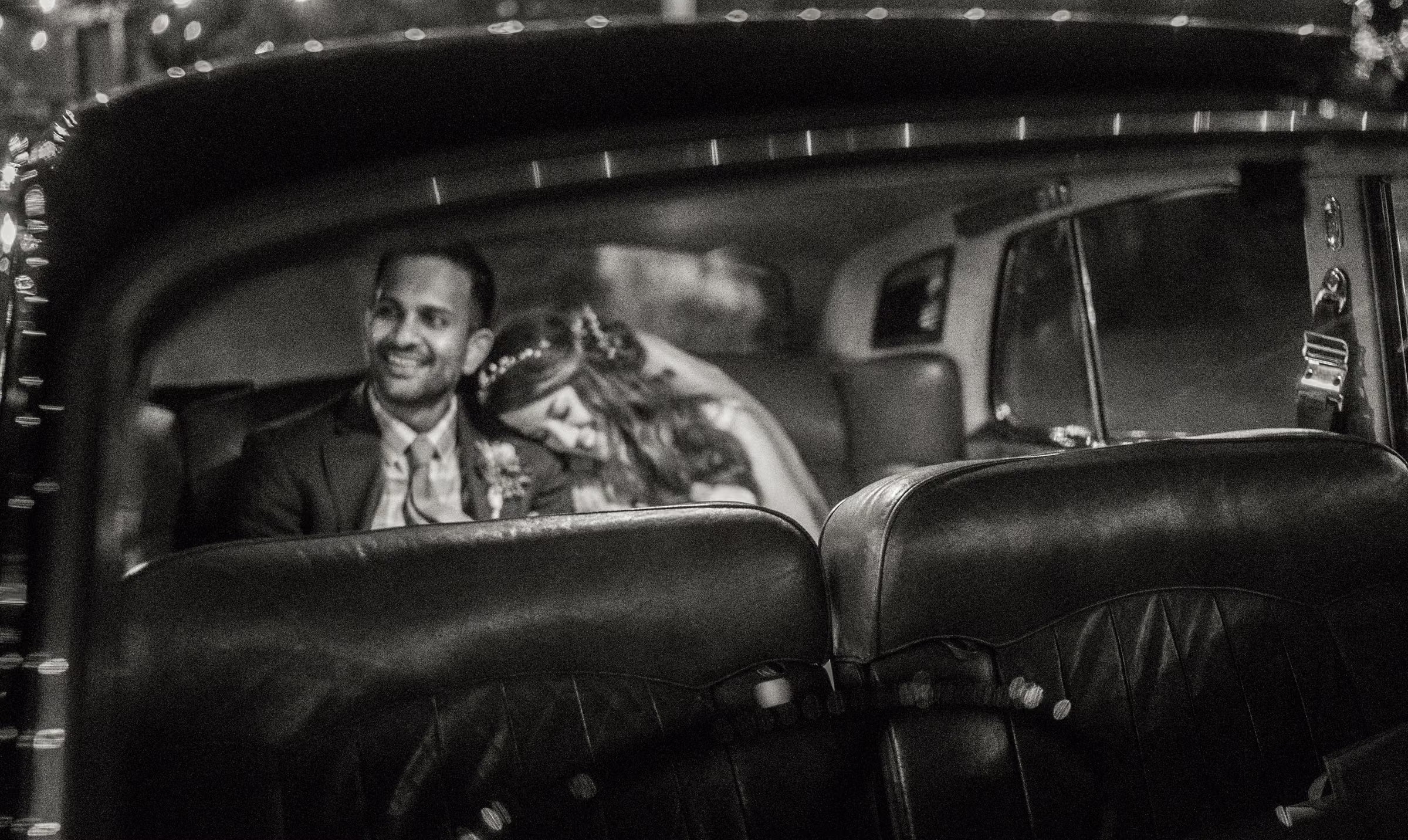 Kash smiles with Kohleen beside him inside the vintage car in a black and white photograph