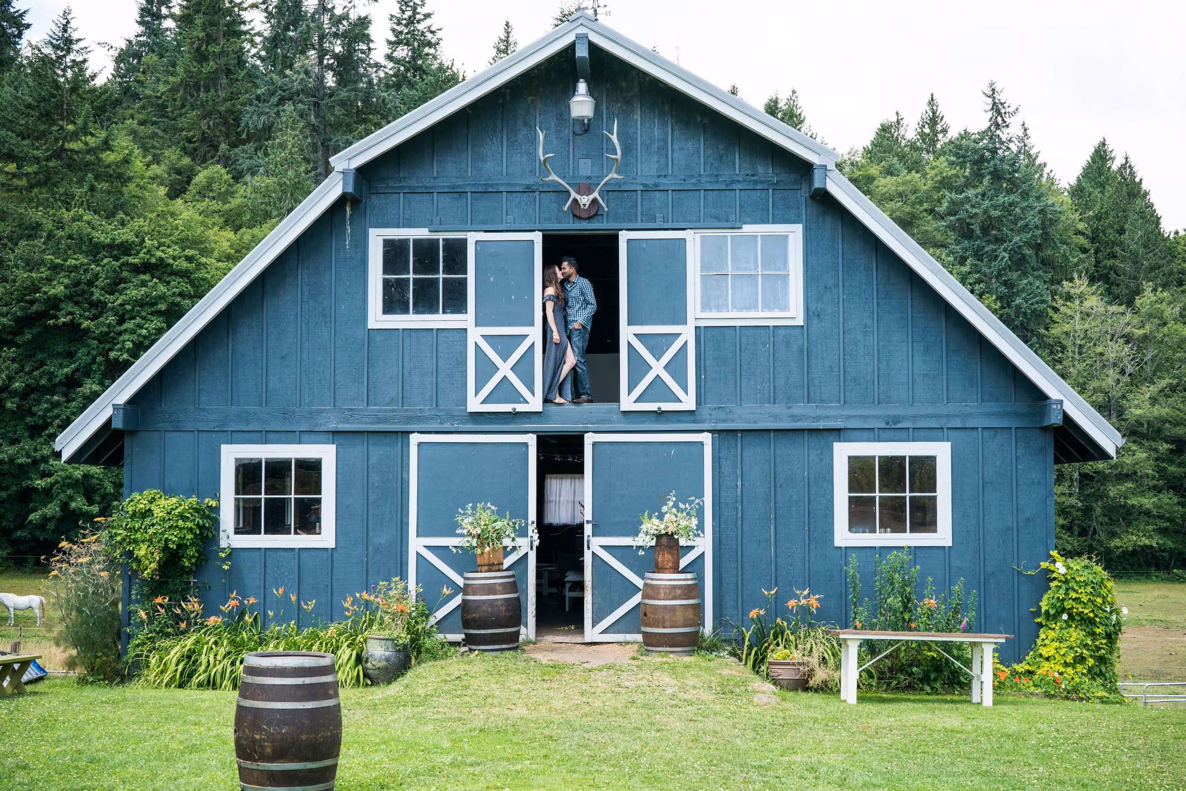 Kohleen and Kash stand together in the open loft doors of the blue barn