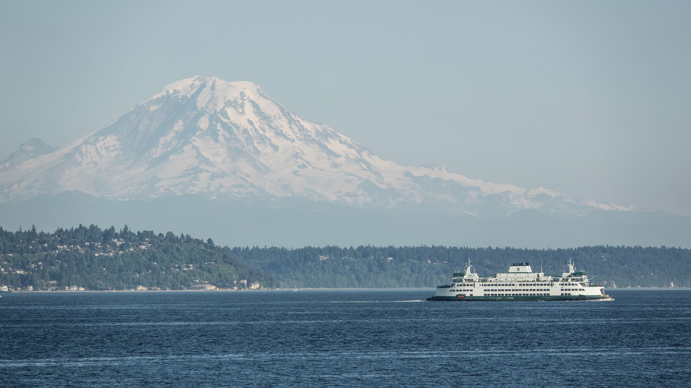 A ferry crosses the water beneath a distant snow-covered mountain in Washington