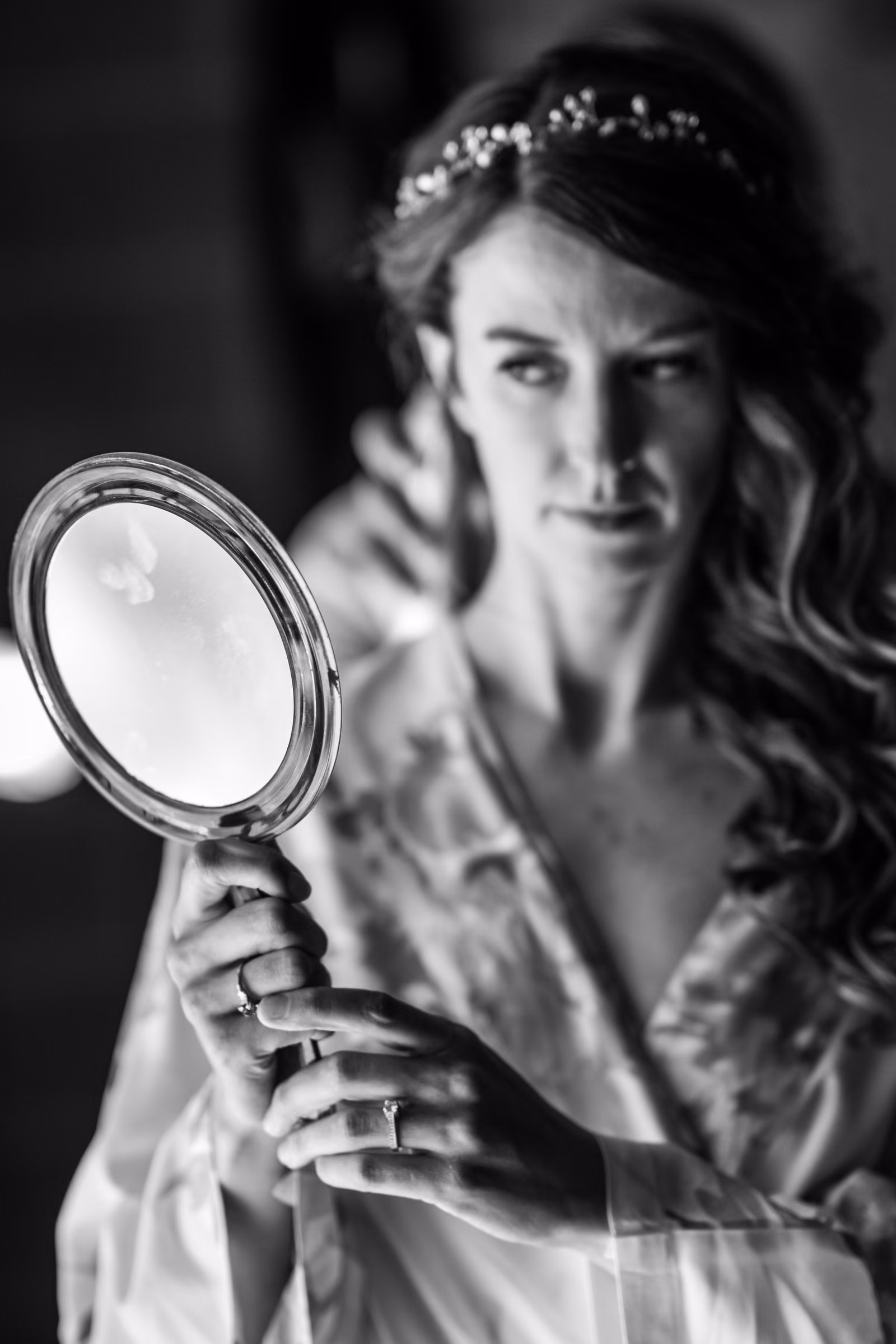 A black and white portrait of Kohleen holding a round mirror with her rings visible on her hands