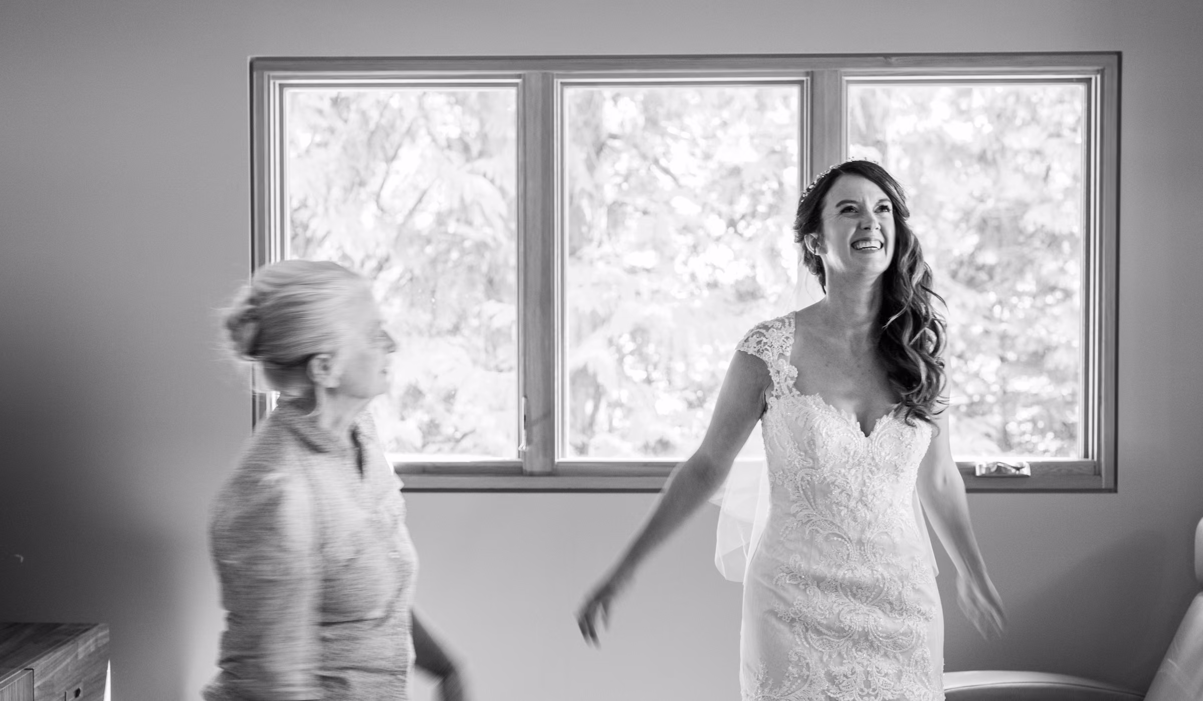 Kohleen laughs in her wedding dress beside her mother near a bright window