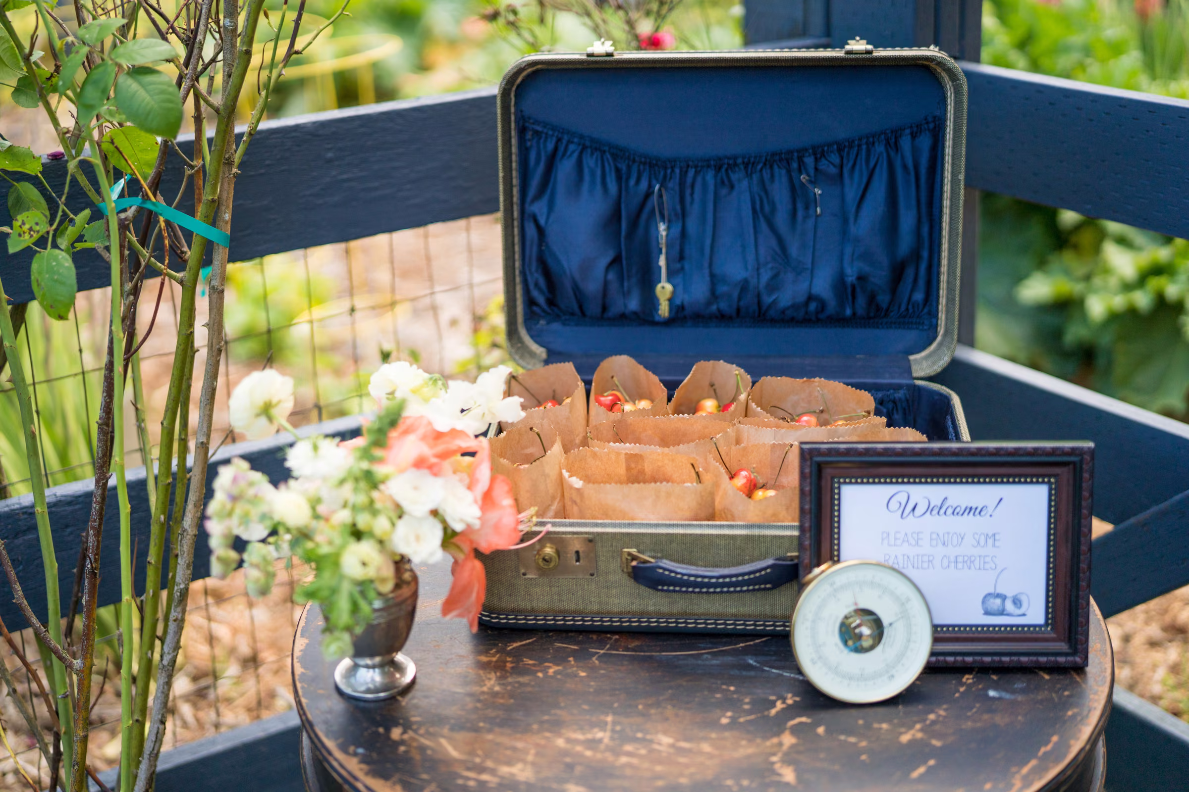 A vintage case with welcome materials, flowers, and a framed sign sits on an outdoor table