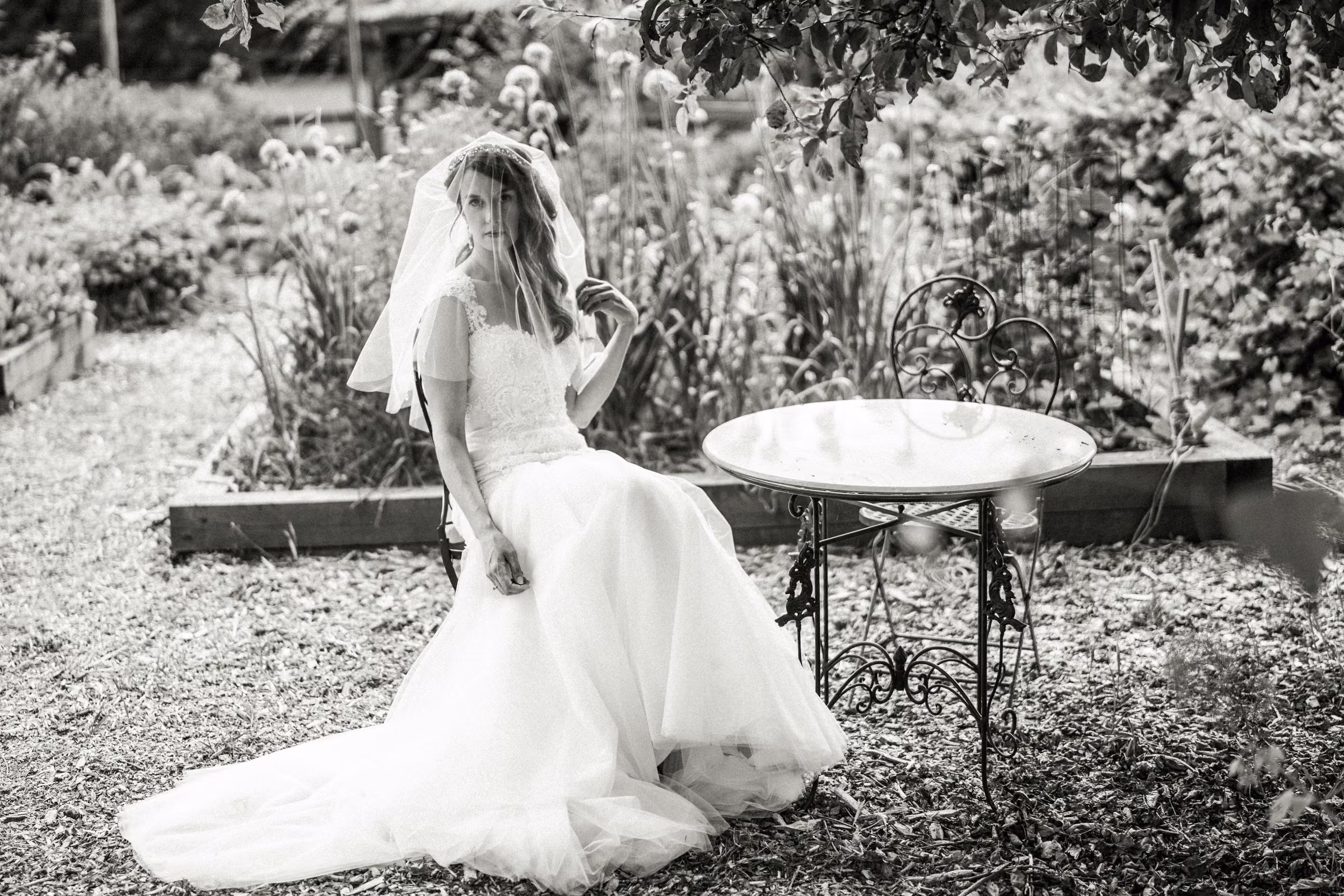 Kohleen sits beside a small garden table in a black and white bridal portrait