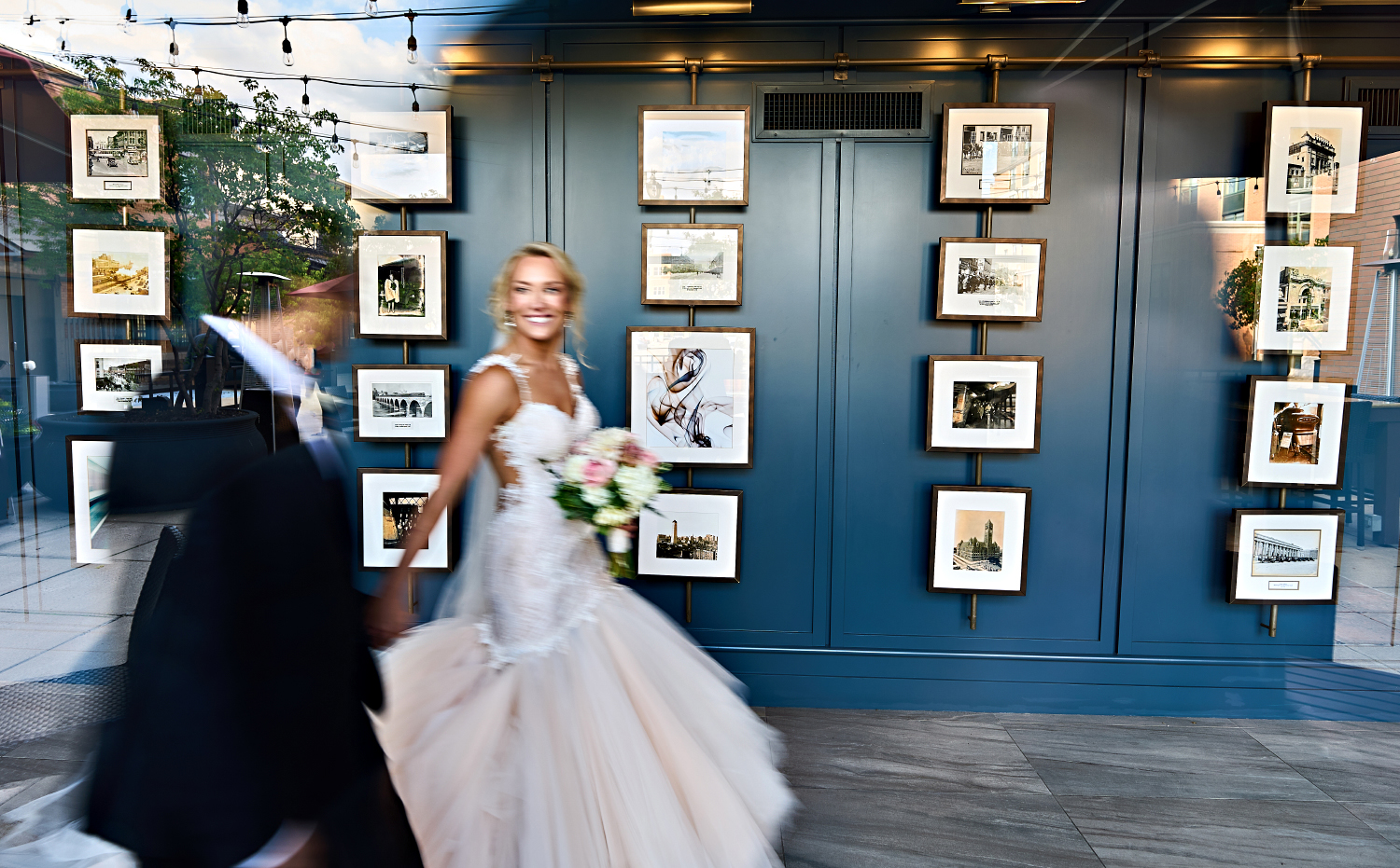 Carrie and Alberto walk through a hallway of framed photographs before their wedding reception