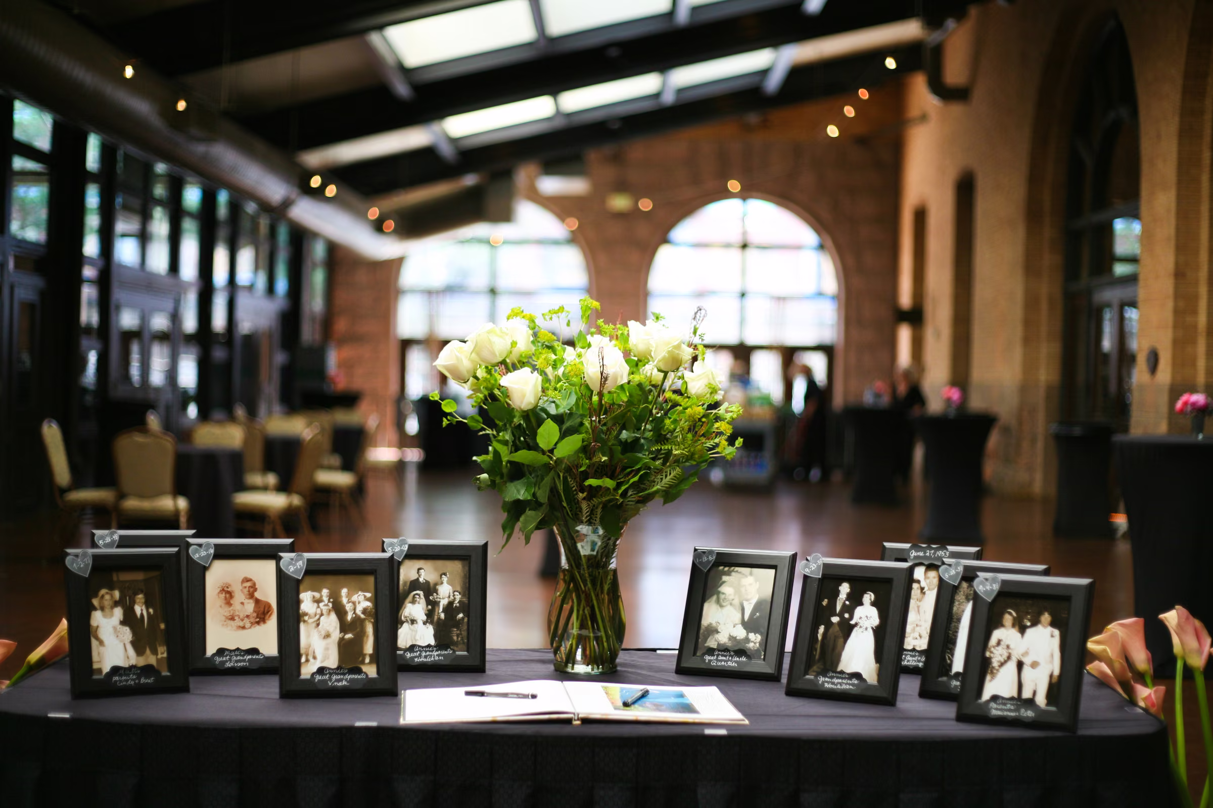 Framed family photographs, white flowers, and guest-book materials fill a welcome table at The Depot