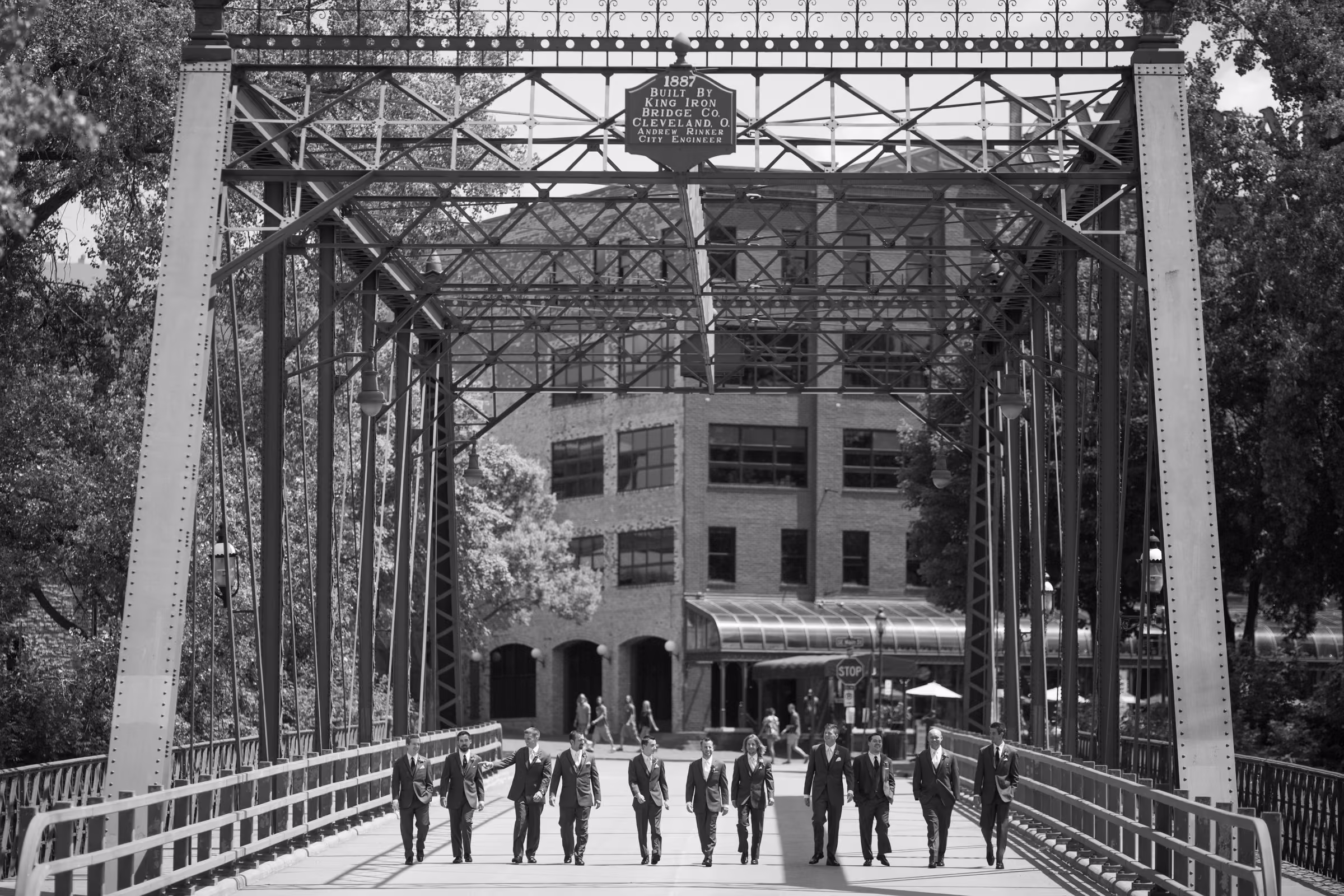 The groom and groomsmen walk beneath the iron trusses and historic sign of Merriam Street Bridge in black and white