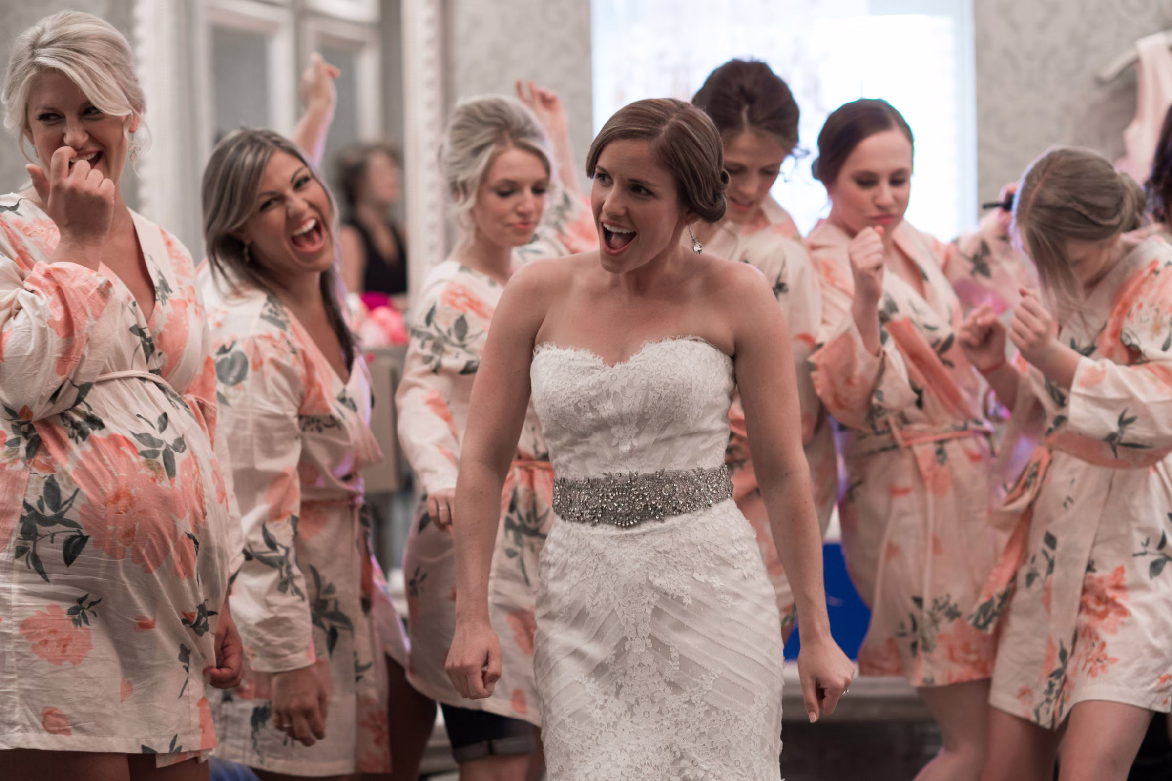 Annie cheers in her wedding dress surrounded by friends in floral robes