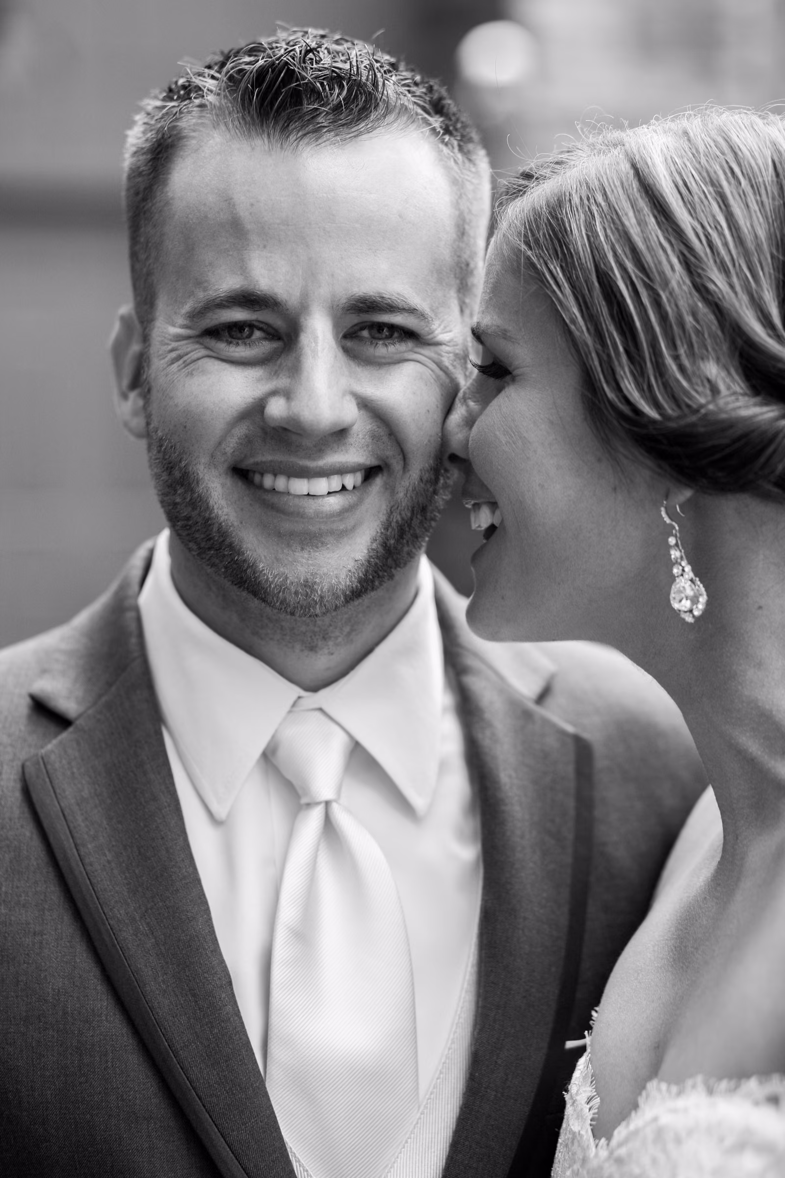 Matt smiles as Annie kisses his cheek in a close black and white portrait