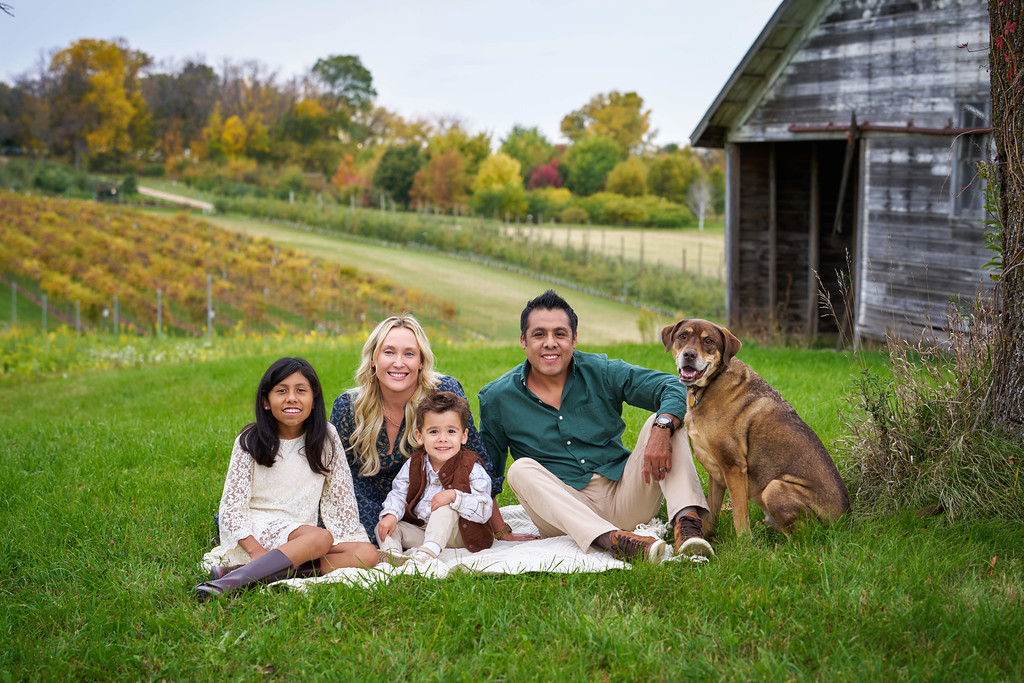 Carrie and Alberto Zaragoza with their two children and dog beside a weathered barn at Minnesota Landscape Arboretum, Chaska, Minnesota